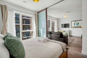 Een moderne hotelkamer met een groot bed, een zithoek, een televisie en uitzicht op de stad.