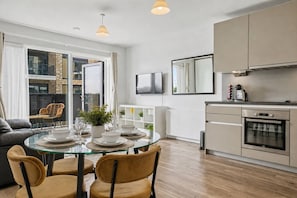 Eine moderne Küche mit Einbauofen, eine Essecke mit Glastisch und Stühlen und ein großes Fenster mit Blick auf die Stadt.