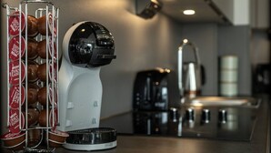 En kaffemaskine med kopholder fyldt med engangskopper, en kaffekande og en elkedel i et moderne køkkenmiljø.