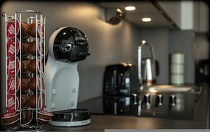 Eine Kaffeemaschine mit Tassenhalter, gefüllt mit Einwegbechern, eine Kaffeekanne und ein Wasserkocher in einer modernen Küche.
