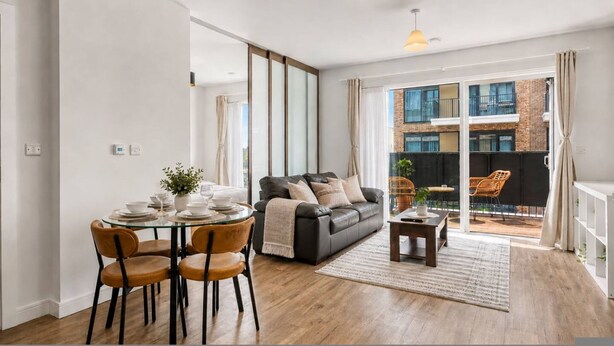 En moderne stue med et glasbord, lædersofa og udsigt til en murstensbygning gennem store vinduer.
