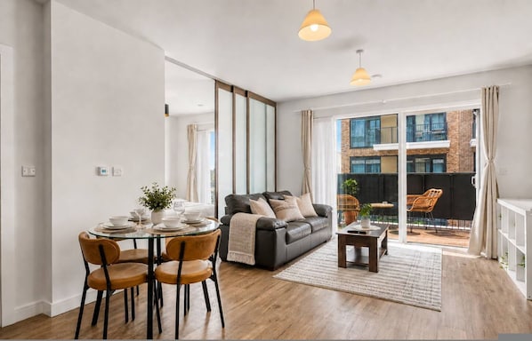 Ein modernes Wohnzimmer mit einem Glastisch, einer Ledersofa und Blick auf ein Backsteinhaus durch große Fenster.