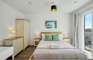 Ein Schlafzimmer mit Bett, Nachttischen, einem Kleiderschrank, einem Gemälde und einem Fenster mit Vorhängen.