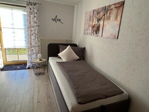 A bedroom with a bed, a small table, a radiator, and a window with curtains. - Vacation apartment Köppl (Lam)