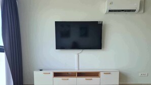 Een moderne woonkamer met een witte televisie aan de muur, een ronde witte salontafel met houten poten en een wit kastje met houten handgrepen.
