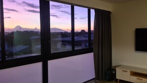 Een kamer met een groot raam, een flatscreen televisie aan de muur en een houten kastje eronder.
