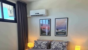 Een slaapkamer met een bed, twee bedlampen, een airconditioner en twee ingelijste foto’s aan de muur.