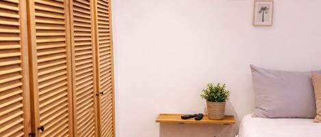 A bedroom with a wooden wardrobe, a bedside table with a plant, and a bed with a blanket.