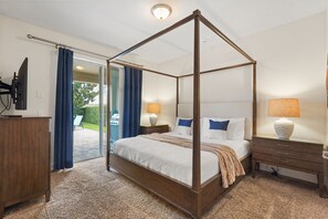 Uma cama com dossel e cortina, uma televisão em um móvel, uma escrivaninha com abajur e vista para um jardim através de uma porta de vidro.