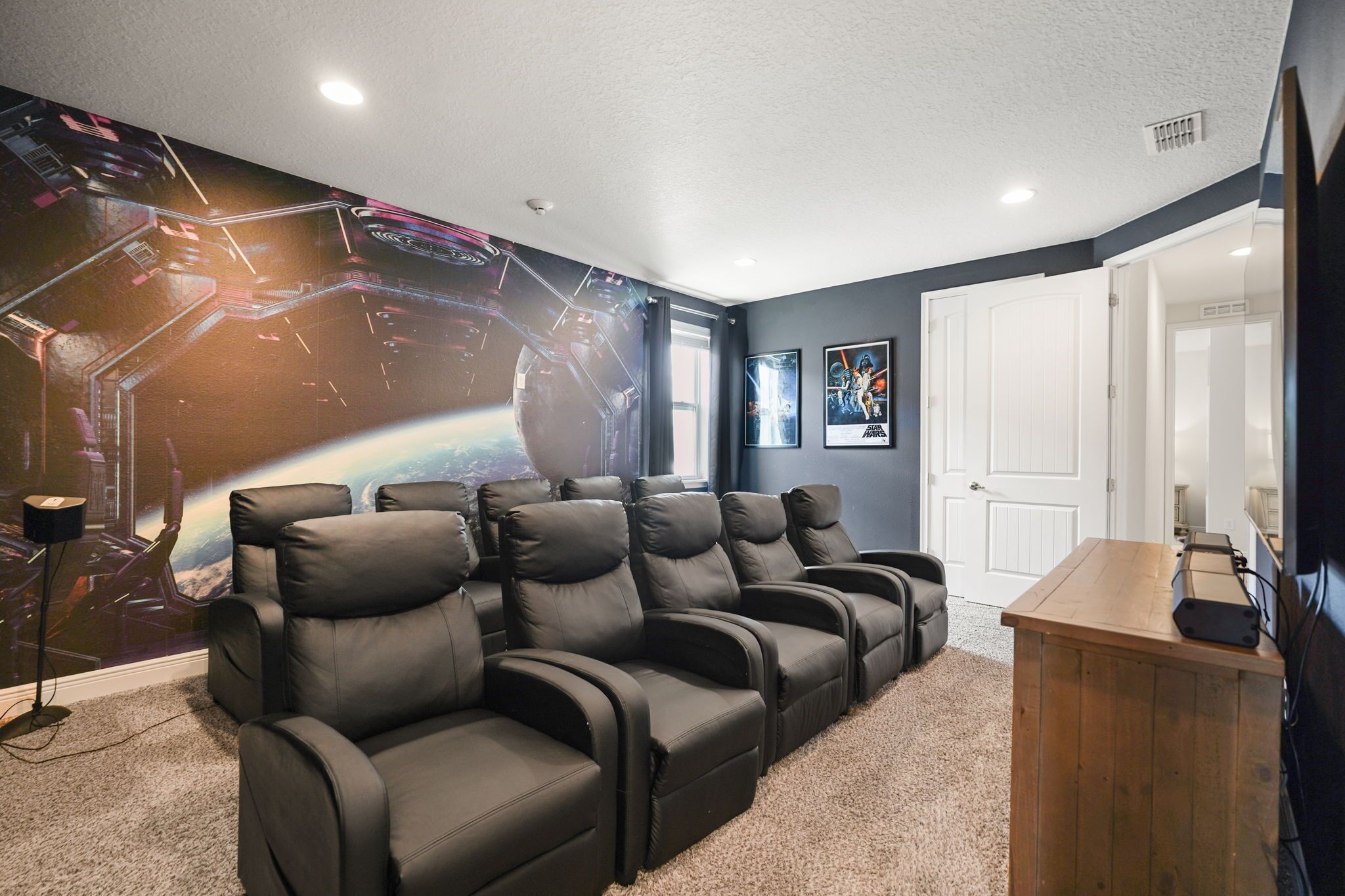 A home theater room with a large wall mural, reclining chairs, a carpeted floor, and a wooden cabinet.