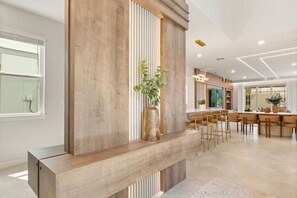 A modern interior with a wooden reception desk, a seating area with bar stools, and a dining table. - 8 BD / 5.5 BA / Windsor Cay 1012 BP (Clermont)