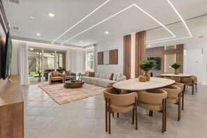 A modern living room with a sofa set, a coffee table, and a dining area with chairs. - 8 BD / 5.5 BA / Windsor Cay 1012 BP (Clermont)