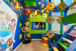 A room with a TV screen displaying a movie, a toy figure, and colorful wall decorations. - 8 BD / 5.5 BA / Windsor Cay 1012 BP (Clermont)