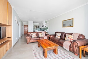 A modern living room with a brown leather sofa, a wooden coffee table, and a striped rug. - Rouxvilla - Two Bedroom Apartment, Sleeps 4 (Jeffreys Bay)