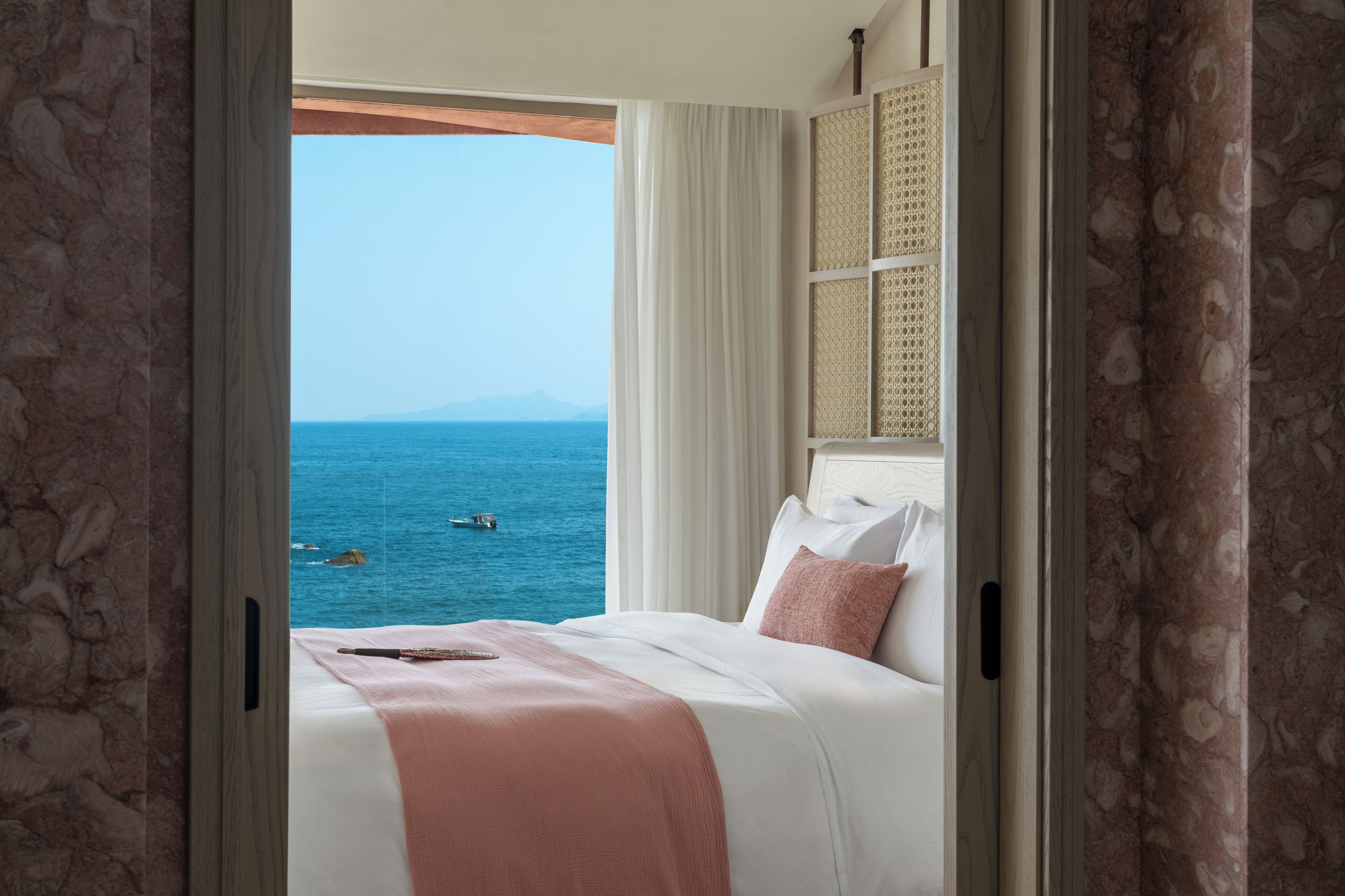 A bedroom with a view of the sea, a bed with white bedding, and a window with a view.