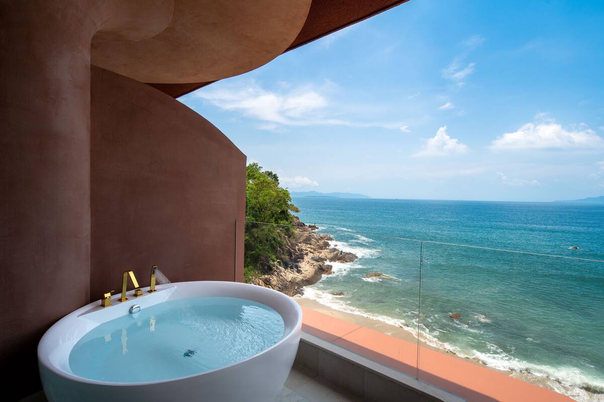Una bañera grande con vista al océano y a la costa rocosa.