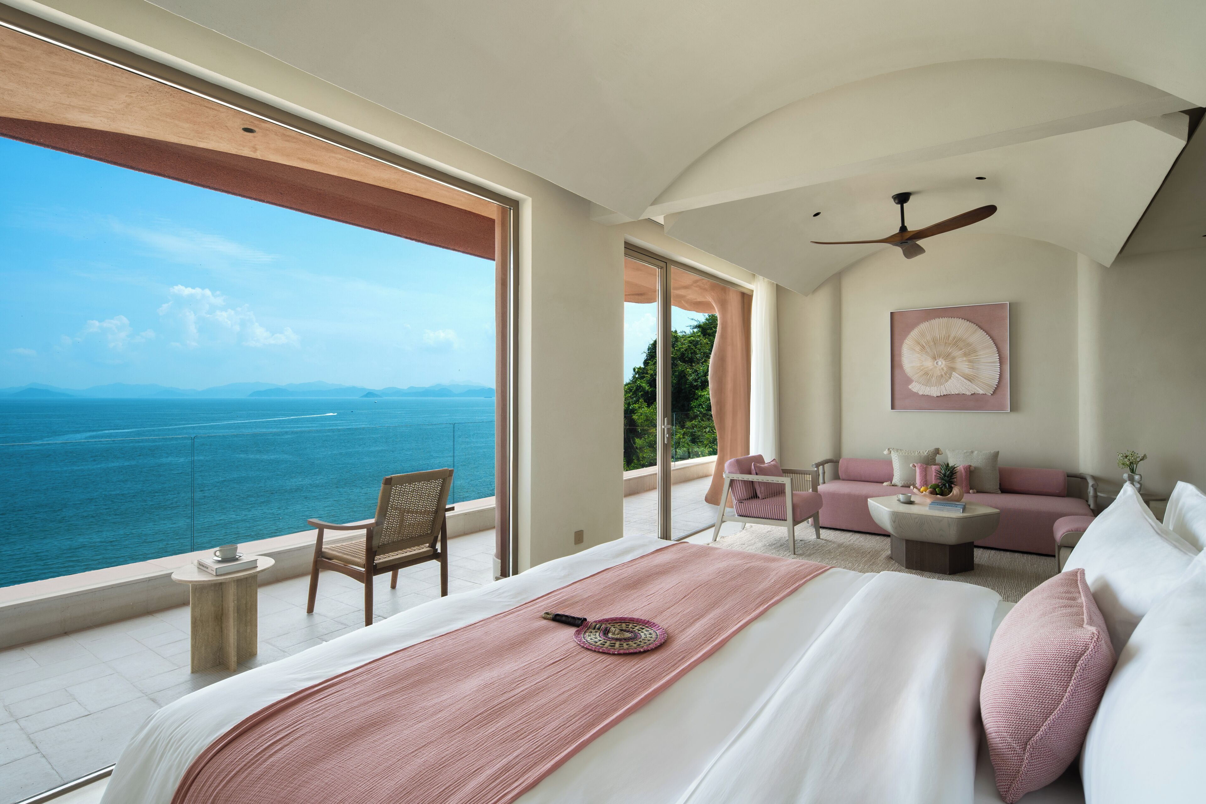 Un dormitorio con una cama grande, vista al mar, un ventilador de techo y un sofá con vista.