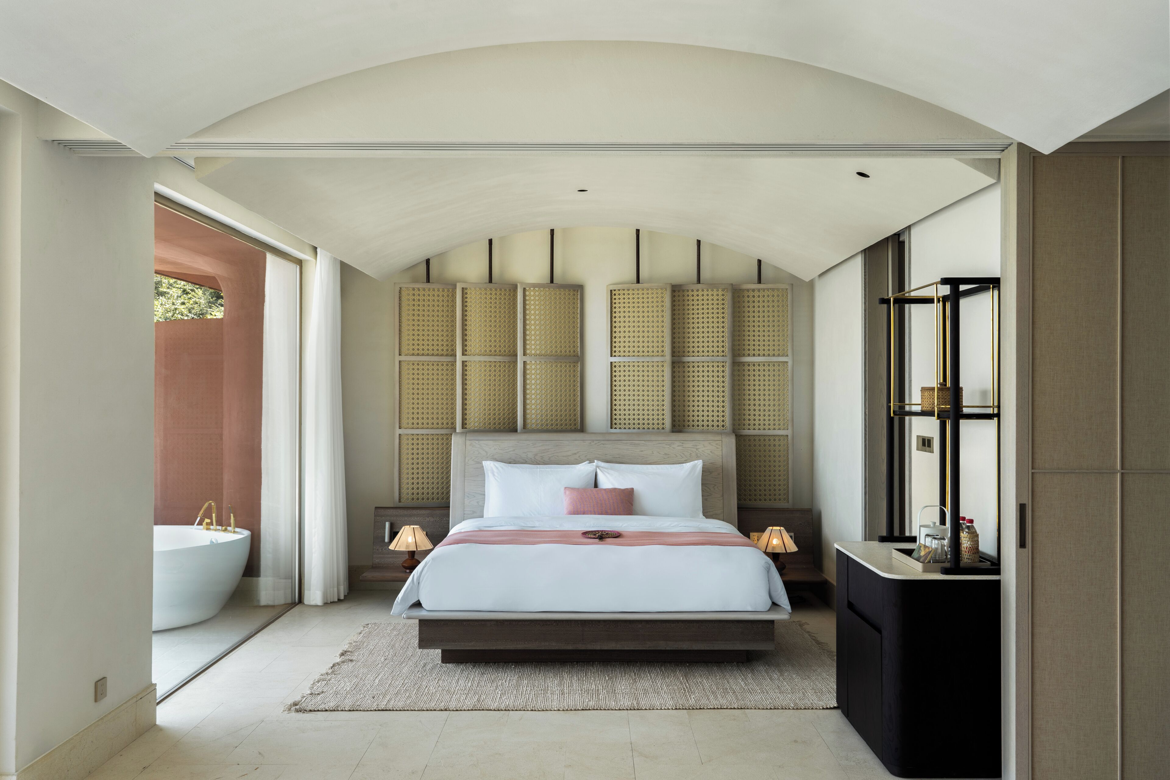 A modern bedroom with a large bed, bedside tables, a built-in bench, and a view of the outside.