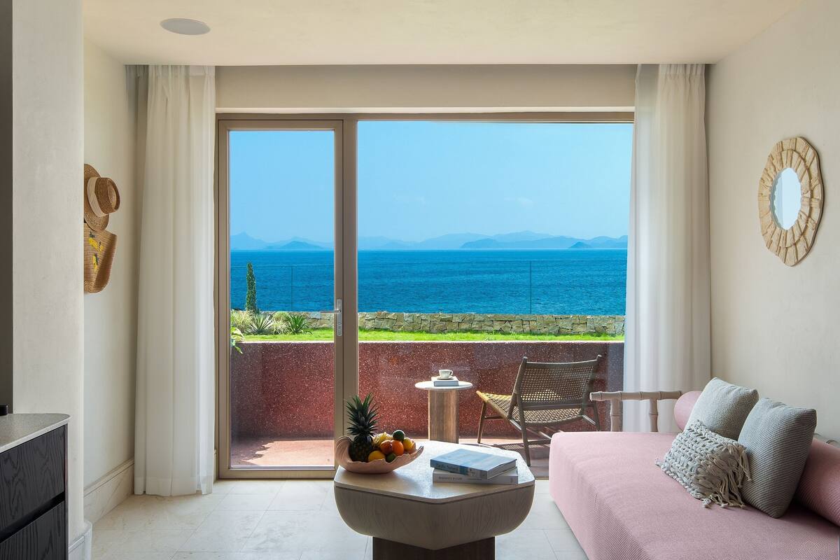 Una habitación con balcón, un sofá, una mesa con frutero y una silla.