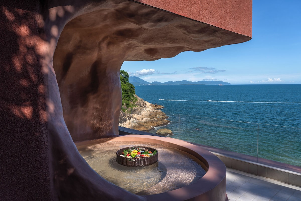 Vista del océano desde un balcón con una chimenea y un muro de piedra.