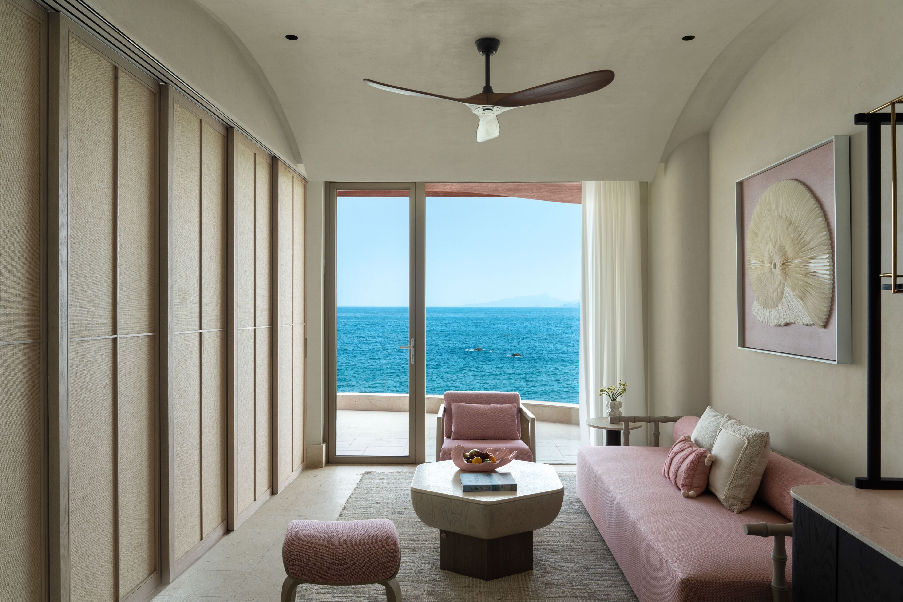 A room with a ceiling fan, a sofa, a table, and a view of the sea.