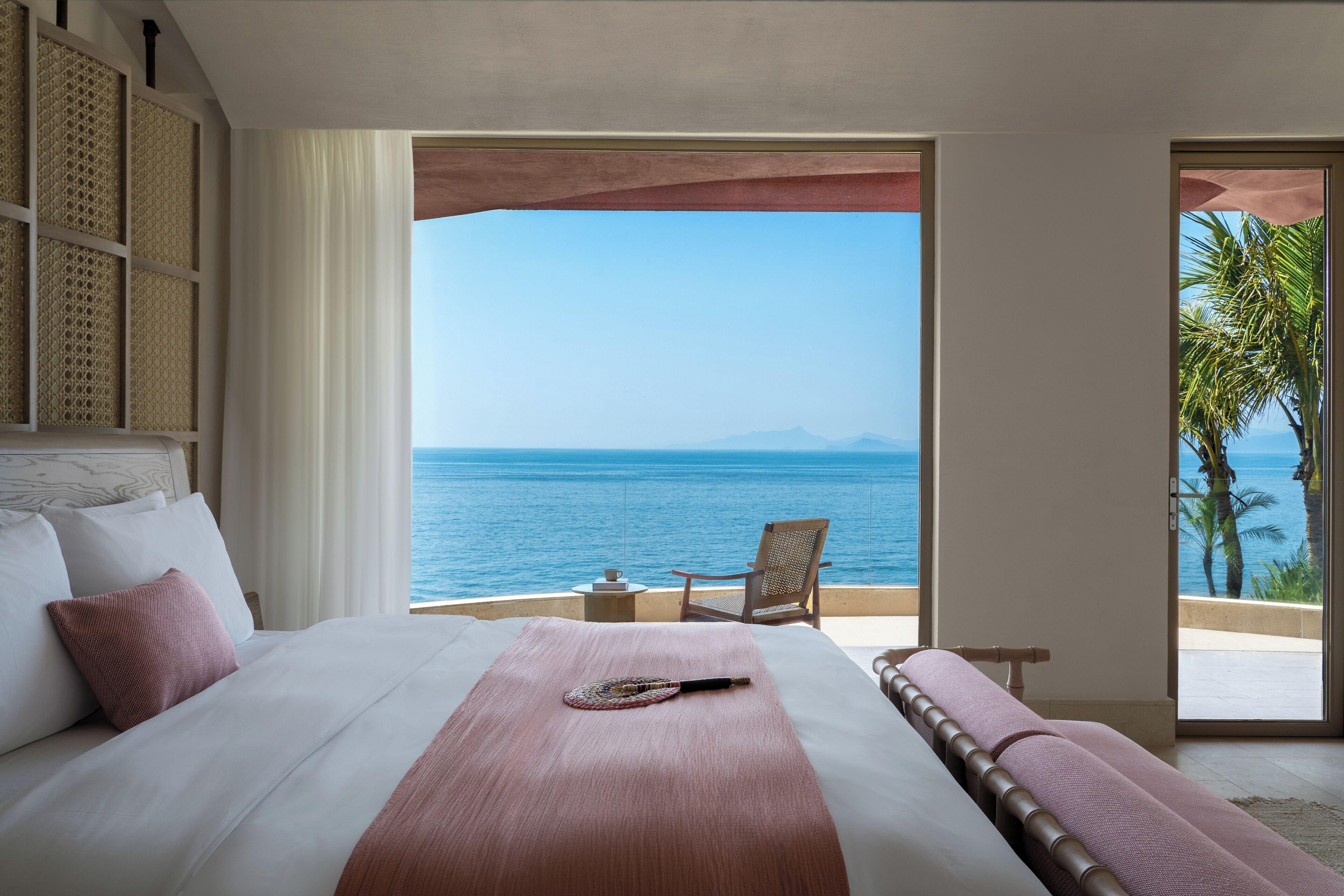 A bedroom with a large bed, a view of the sea, a chair, and a small table.