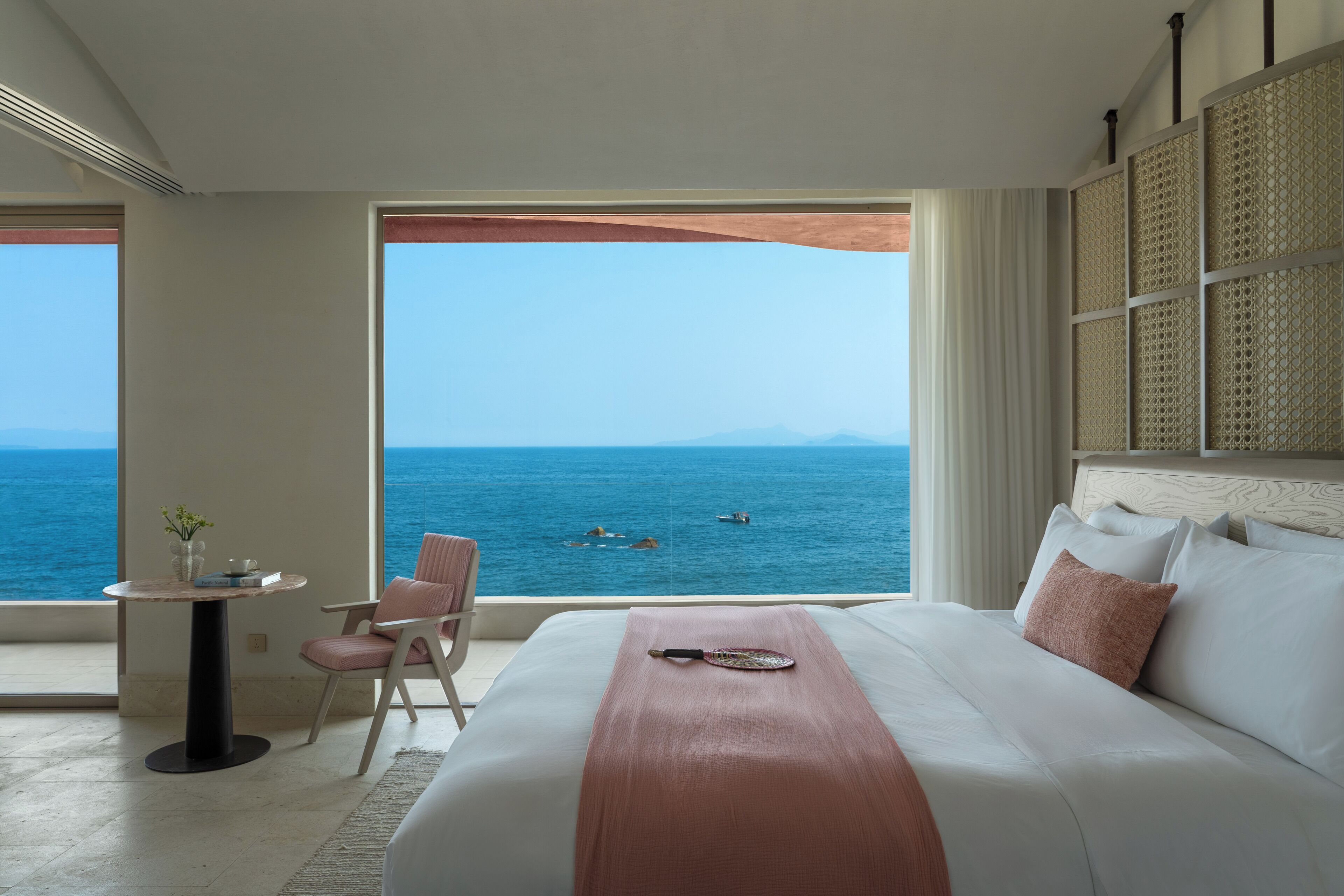 A hotel room with a large window, a bed, a small table, and a chair.