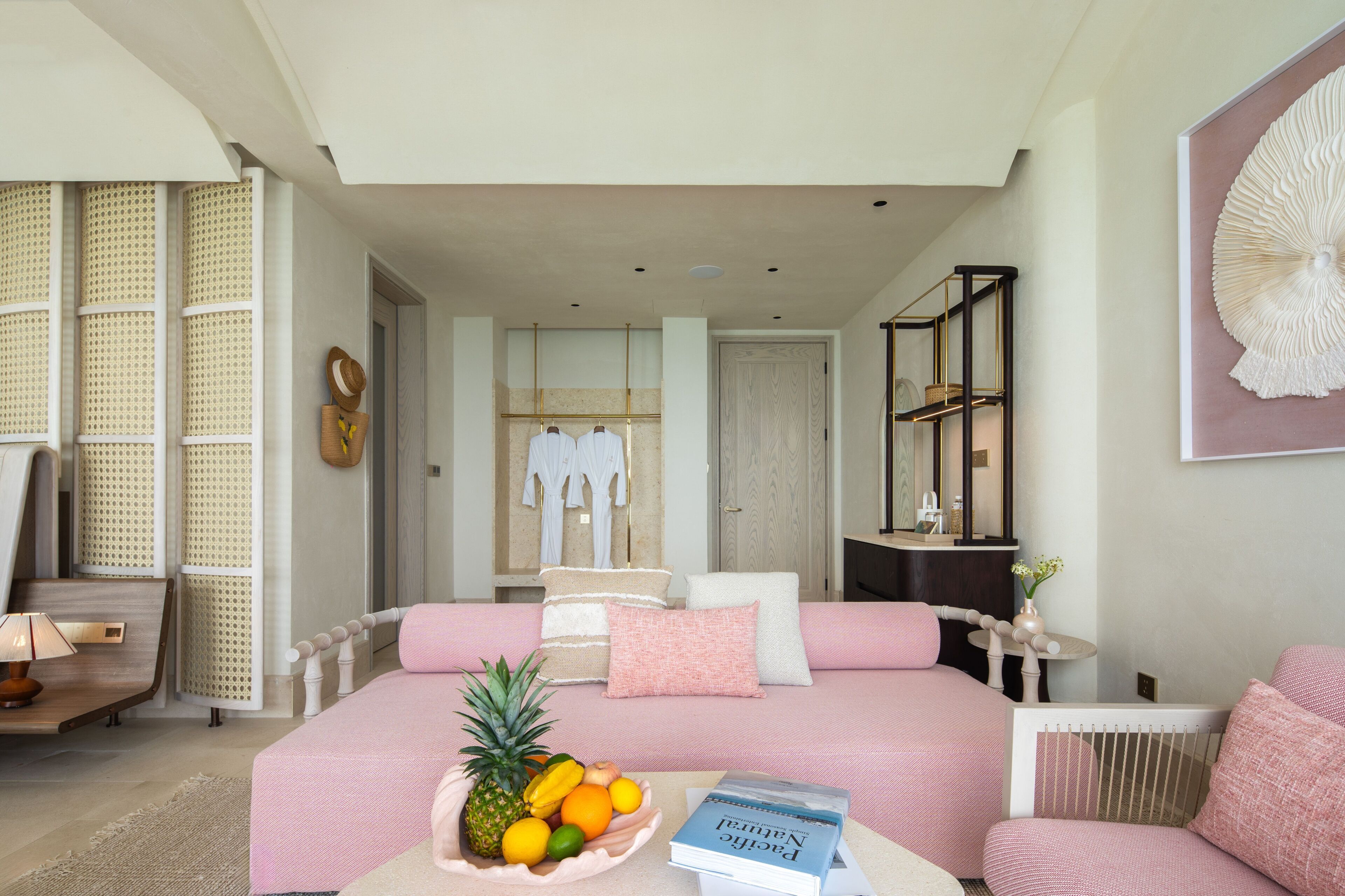 A modern bedroom with a pink bed, a fruit bowl, and a book on the bedside table.