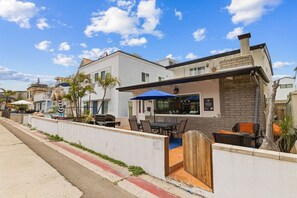 A modern building with a patio area featuring outdoor seating and a barbecue grill. - South Mission Beach Home – 3BR, Epic Patio, Rare 3-Car Parking, Steps to the Sand (San Diego)