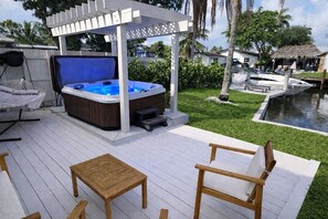 Una vasca idromassaggio sotto una pergola, un pontile in legno e un'area piscina con lettini da relax.