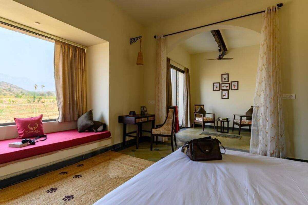 Quarto de hotel com cama, escrivaninha, cadeira, janela com cortinas e vista para o exterior.