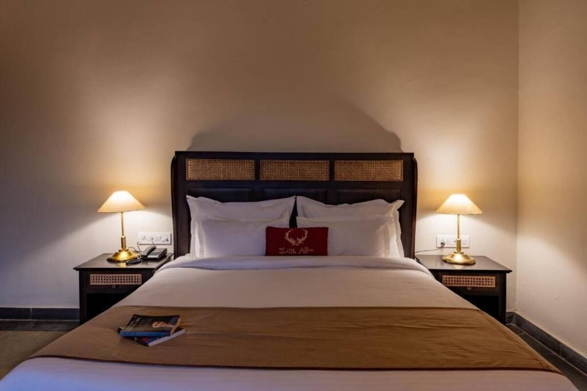 Uma cama bem arrumada com um travesseiro vermelho, duas luminárias de cabeceira e um livro sobre a cama.