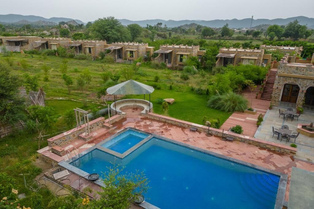 A pool area with a clear view of the surrounding landscape, including a series of traditional-style buildings and a grassy field.