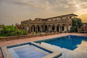 A pool area with a stone building, arched walkways, and outdoor seating.
