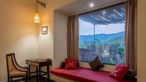 Una habitación con un banco rojo, una mesa, una silla y vistas a un paisaje montañoso por la ventana.