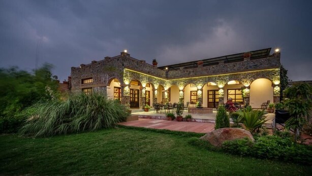 Un edificio de piedra con patio, ventanas de arco y mesas al aire libre.
