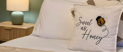 A bed with white bedding, a pillow with 'Sweet as Honey' text, a bee decoration, and a bedside lamp.