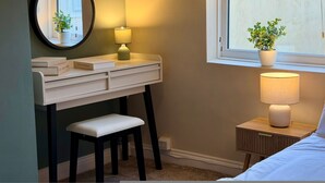 A bedroom with a bed, a bedside table with a lamp, a small stool, a desk with a mirror, and a window with a view of the outside. - South Shields 3BR House Sleeps 6 Great for Group Stays (South Shields)