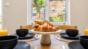 Una presentación para el desayuno con croissants en un soporte, cuencos negros y vasos de zumo de naranja.
