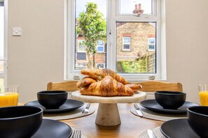 Une table de petit-déjeuner avec des croissants présentés sur un présentoir, des bols noirs et des verres pour le jus d’orange.