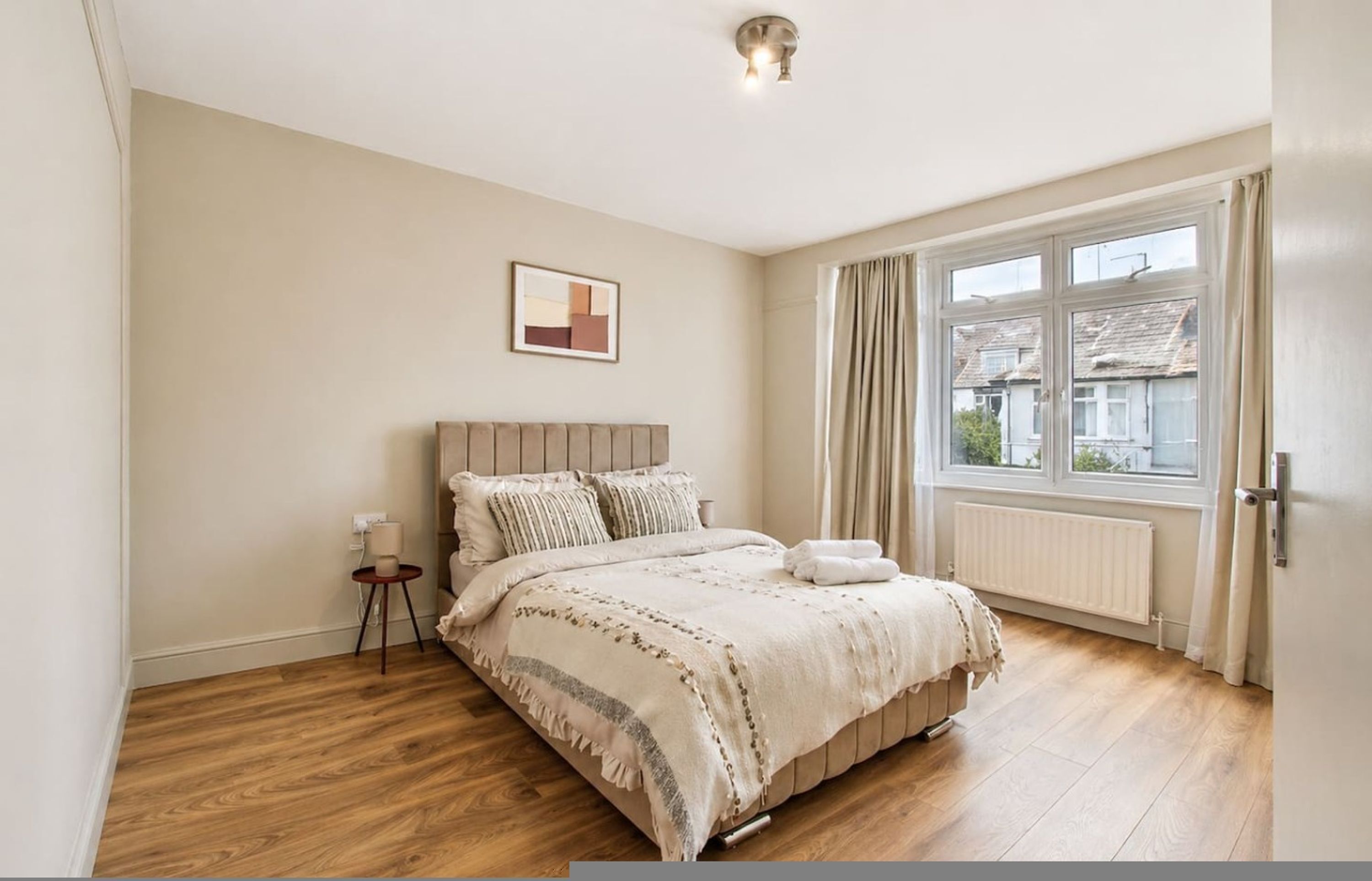 A bedroom with a bed, a bedside table, a window with curtains, and a radiator.