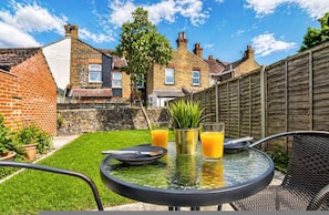 Une terrasse avec une table, des chaises et un verre de jus d’orange.
