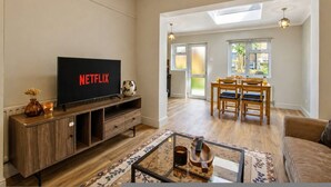 Una sala de estar con televisión, muebles de madera, una mesa de centro de vidrio y una zona de comedor con mesa y sillas.