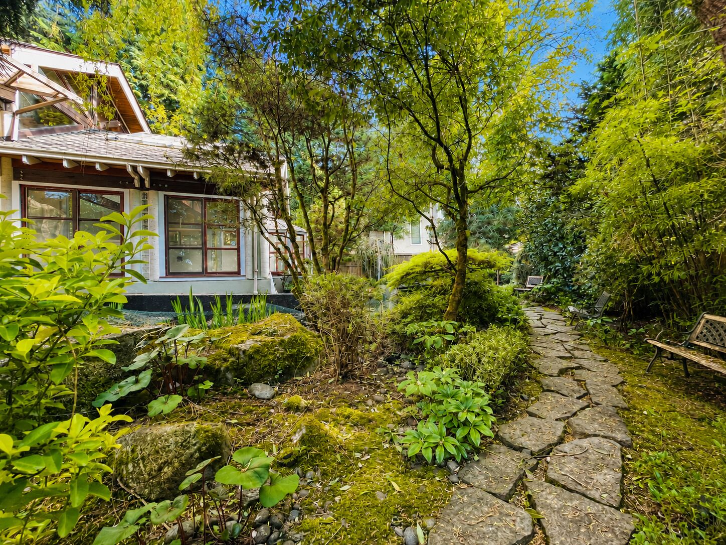 Une maison avec un chemin de pierre menant à l’entrée, entourée d’une végétation luxuriante et d’arbres.