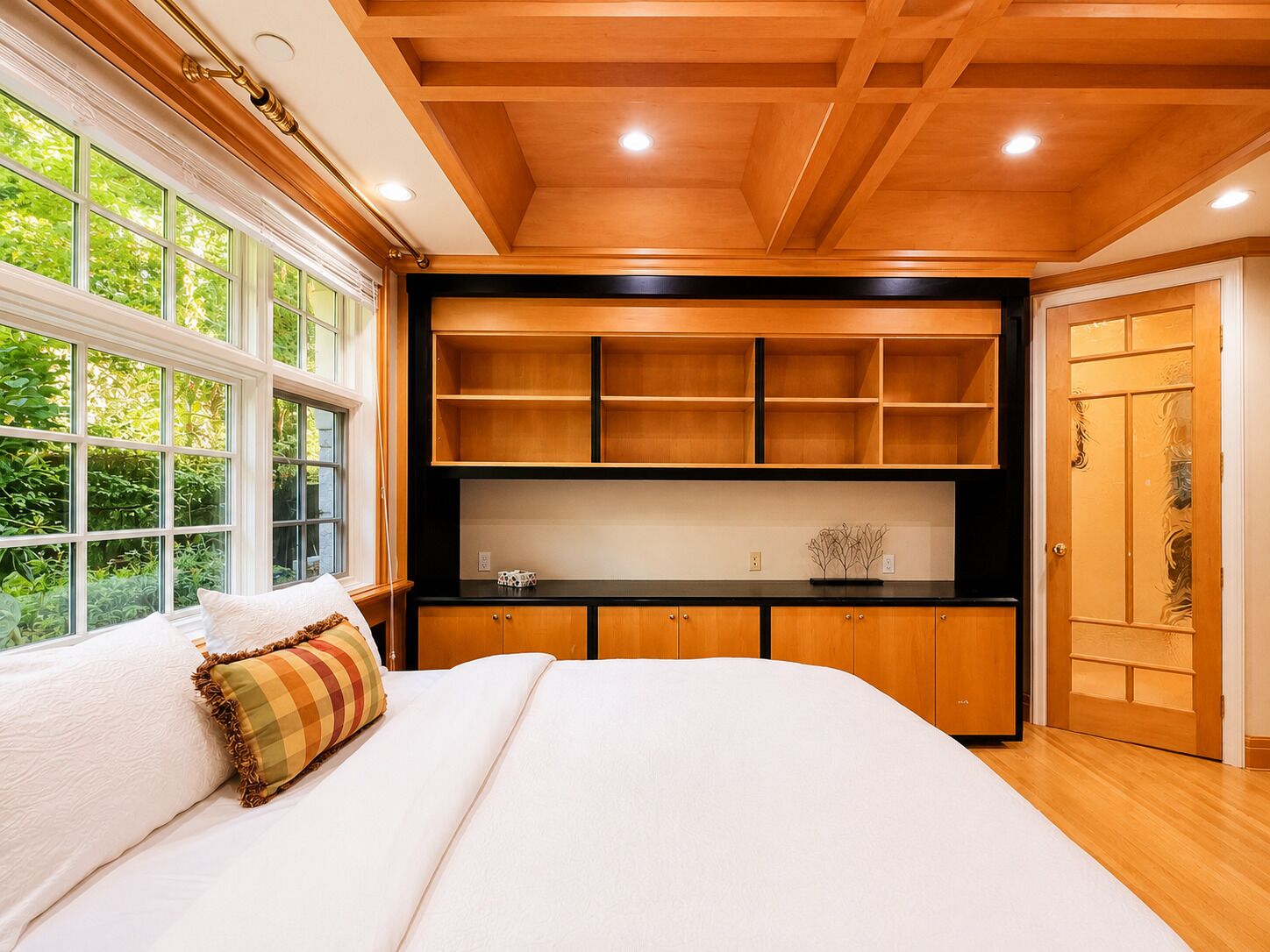 Ein Schlafzimmer mit einem großen Bett, eingebauten Regalen, einem Fenster mit Blick auf Grünflächen und einer Holzbalkendecke.