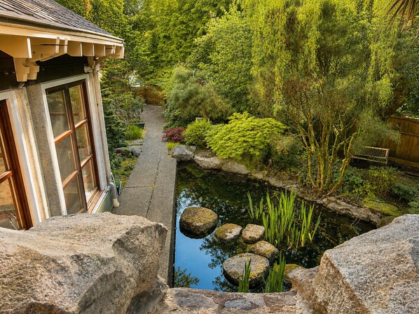 A traditional Japanese-style building with a stone pathway leading to a pond with rocks and greenery.