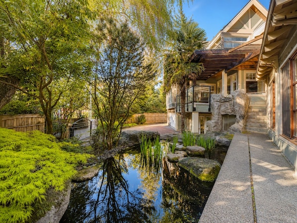 A serene garden with a pond, stone pathway, and a building with a balcony.