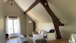 A loft-style room with a sloped ceiling, a wooden beam, a sofa, a table, and a chair. - Maison classée 3 étoiles Parc du Manoir (Amboise)