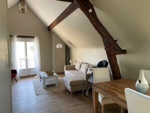 Ein Loft-Zimmer mit schräg verlaufender Decke, einem Holzbalken, einer Couch, einem Tisch und einem Stuhl.