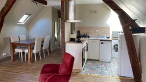 An attic-style room with a dining table, chairs, a red chair, a kitchen with a washing machine, and a skylight. - Maison classée 3 étoiles Parc du Manoir (Amboise)
